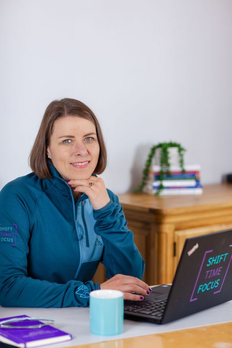 image of Alicja sat at desk in front of laptop with Shift Time Focus stickers on it