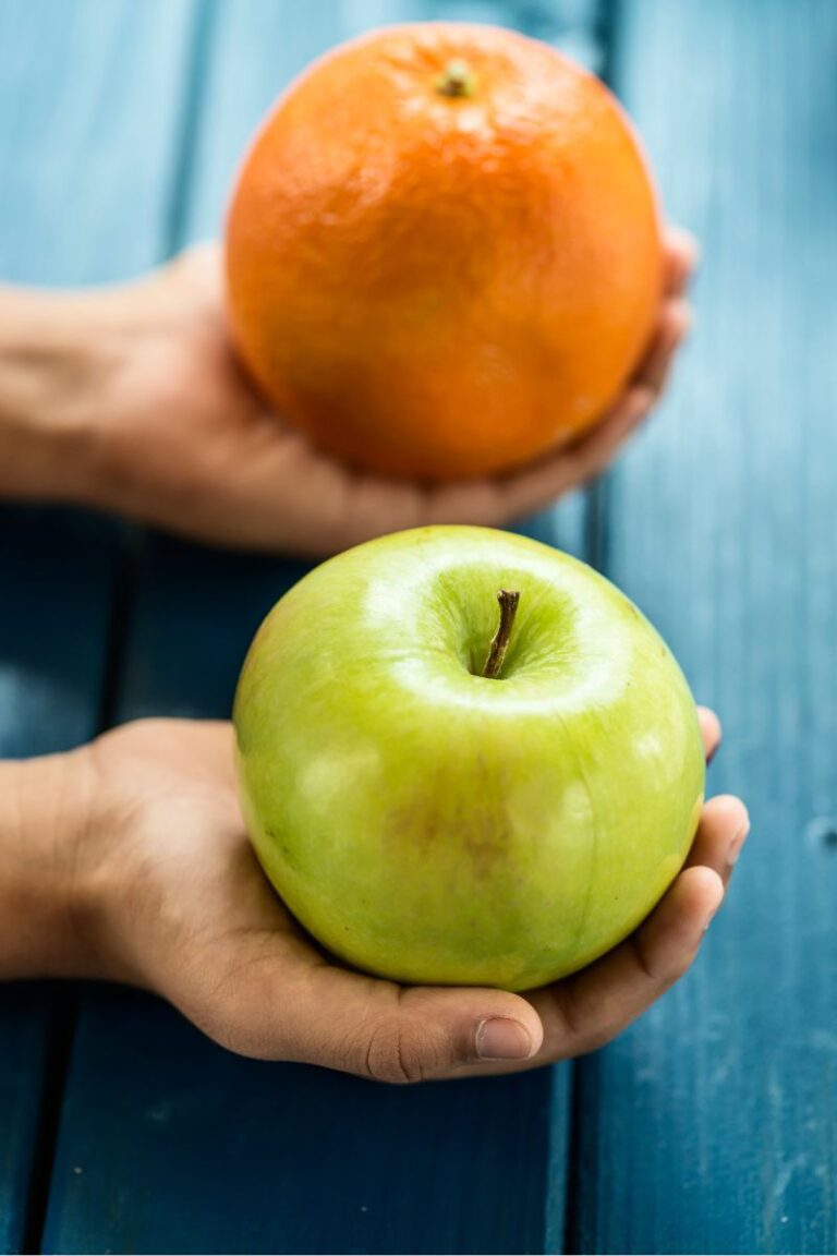 Image of hands, one holding an apple and the other an orange