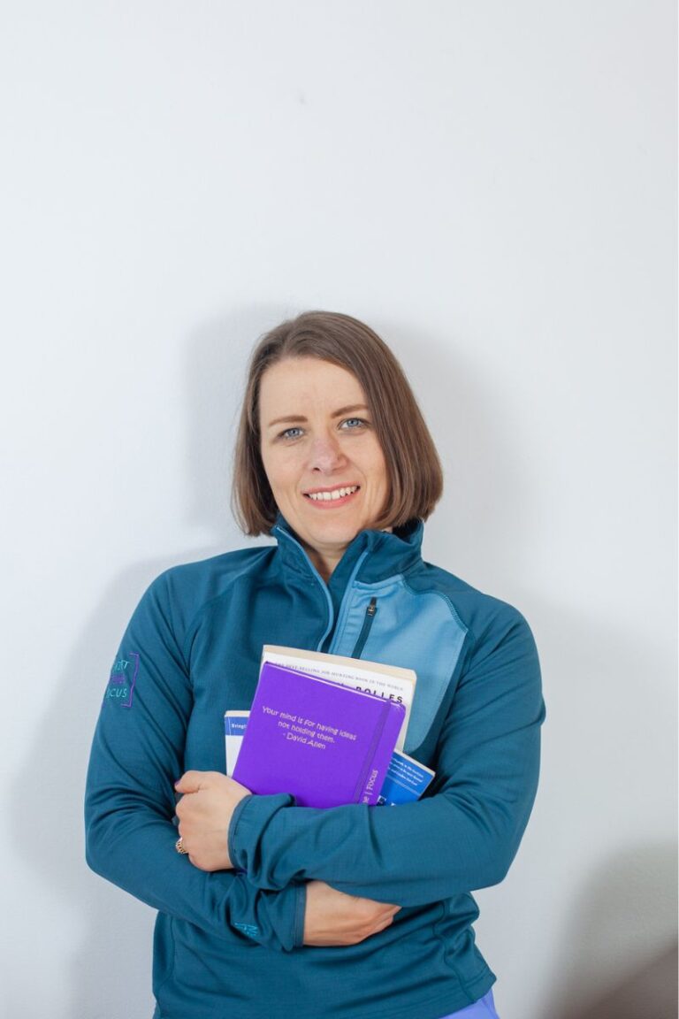 Image of Alicja holding notebook and a selection of books smiling at camera